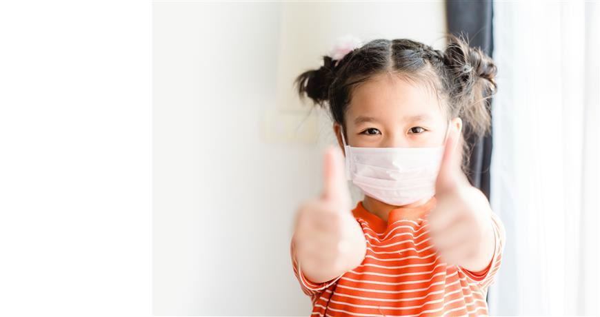 AAPI child wearing a mask giving a thumbs up